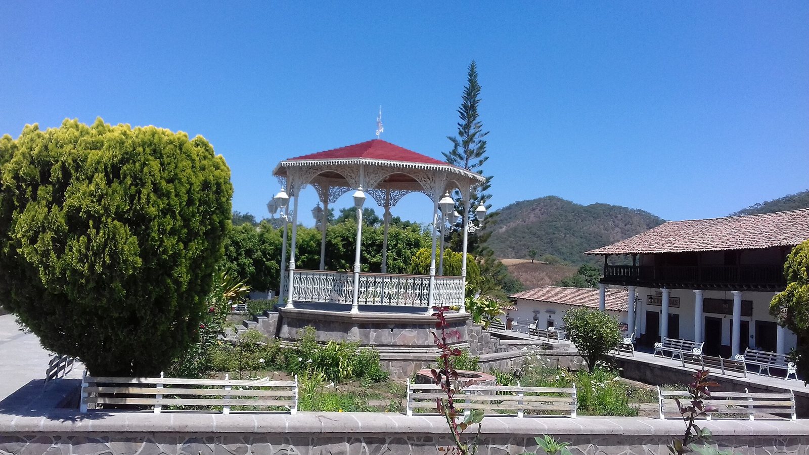 White gazebo with a red roof in the main plaza of San Sebastián del Oeste, surrounded by gardens and benches