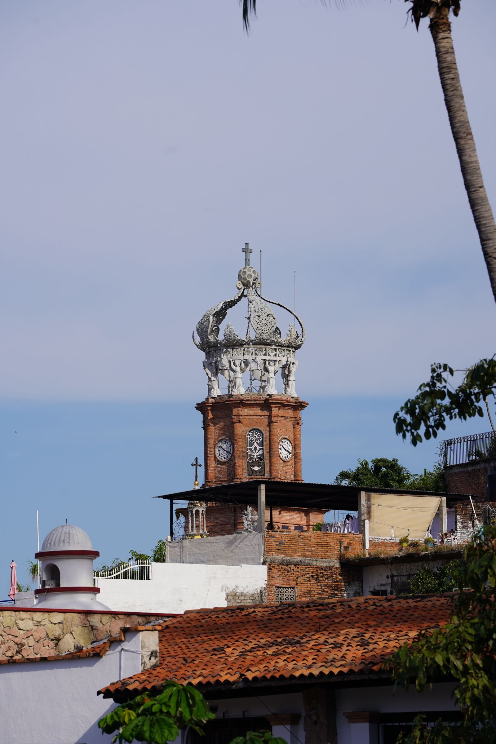 Brick clock tower with the white crown of the Church of Our Lady of Guadalupe above downtown tile roofs