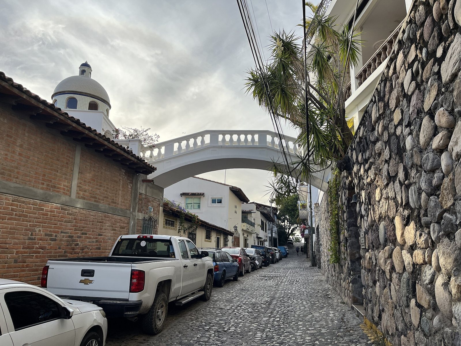 Cobblestone street in downtown Puerto Vallarta with a white balustraded bridge crossing overhead between two houses
