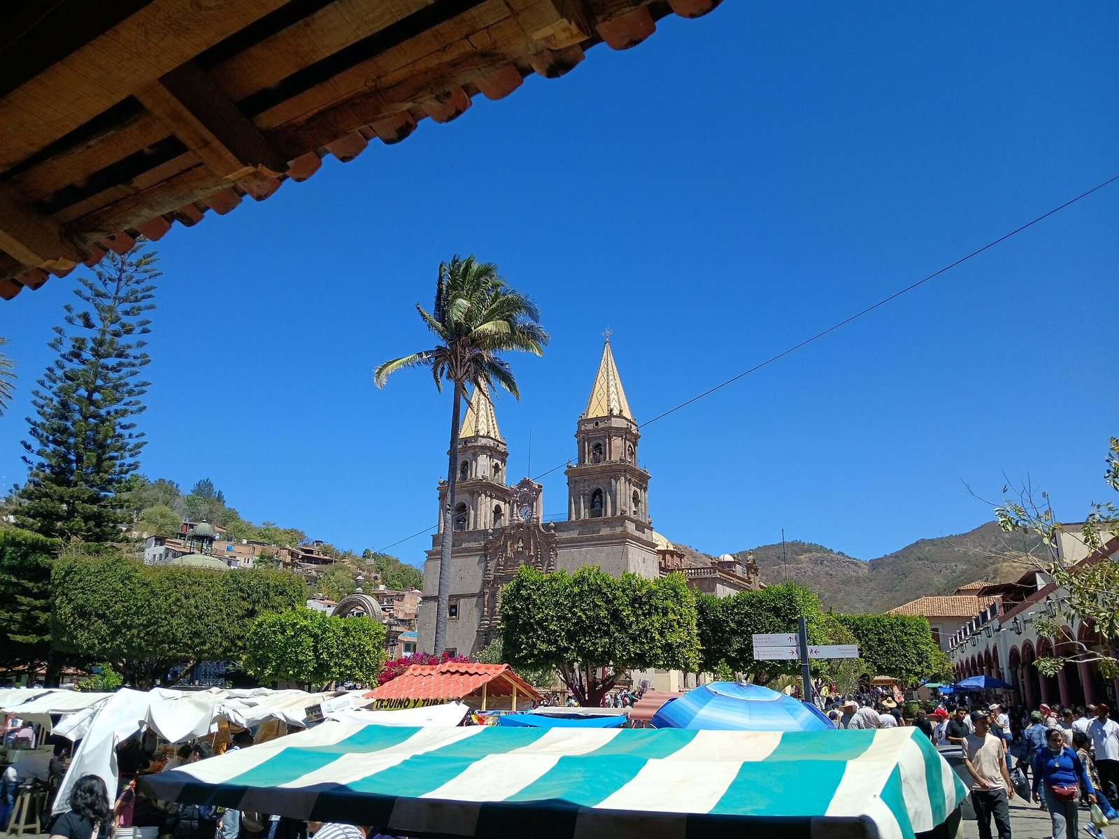 The twin stone towers of the Basilica of Our Lady of the Rosary in Talpa de Allende behind a palm tree and market stalls
