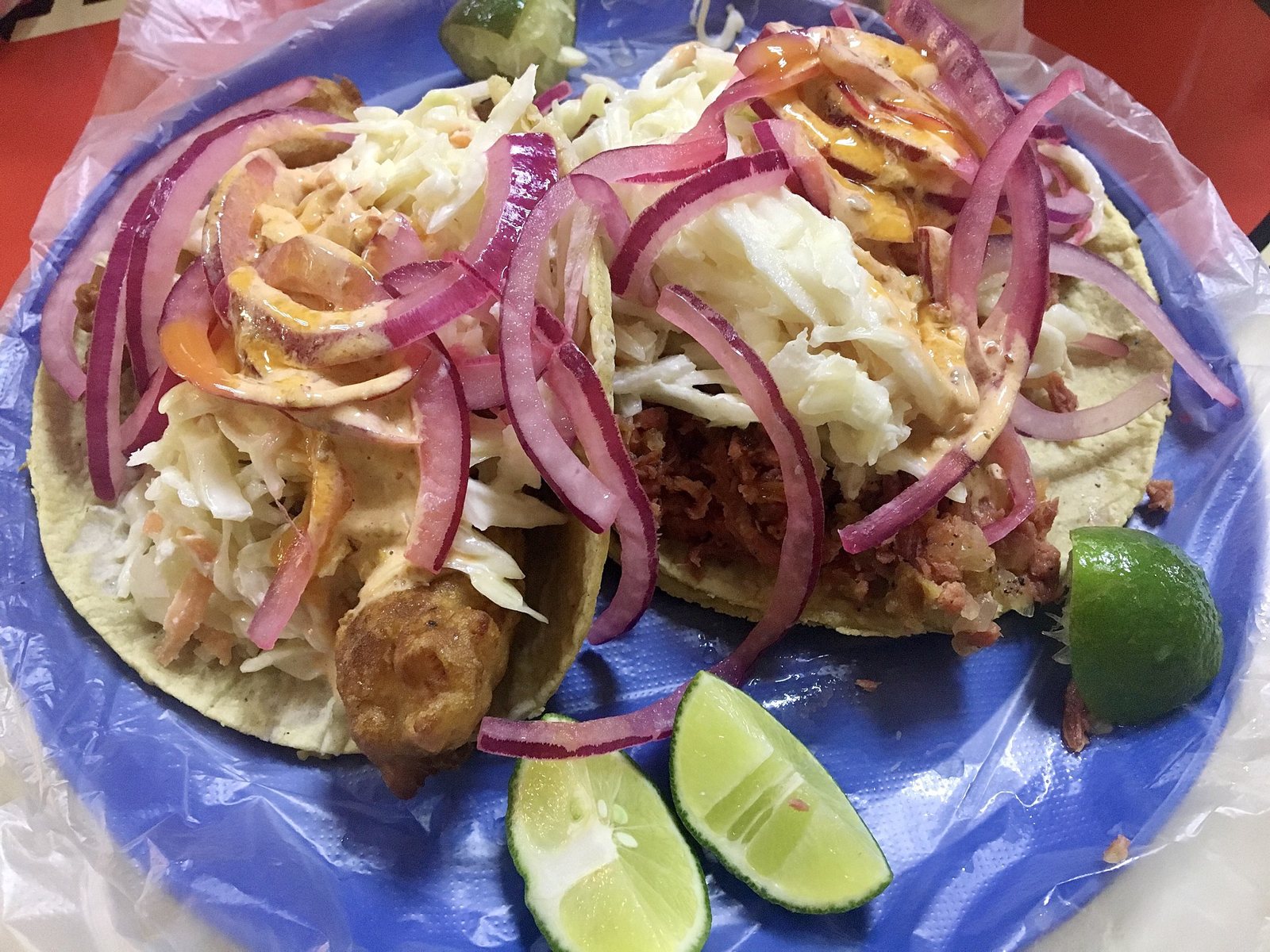 Two battered fish tacos topped with cabbage, red onion and creamy sauce, with lime wedges on a plate