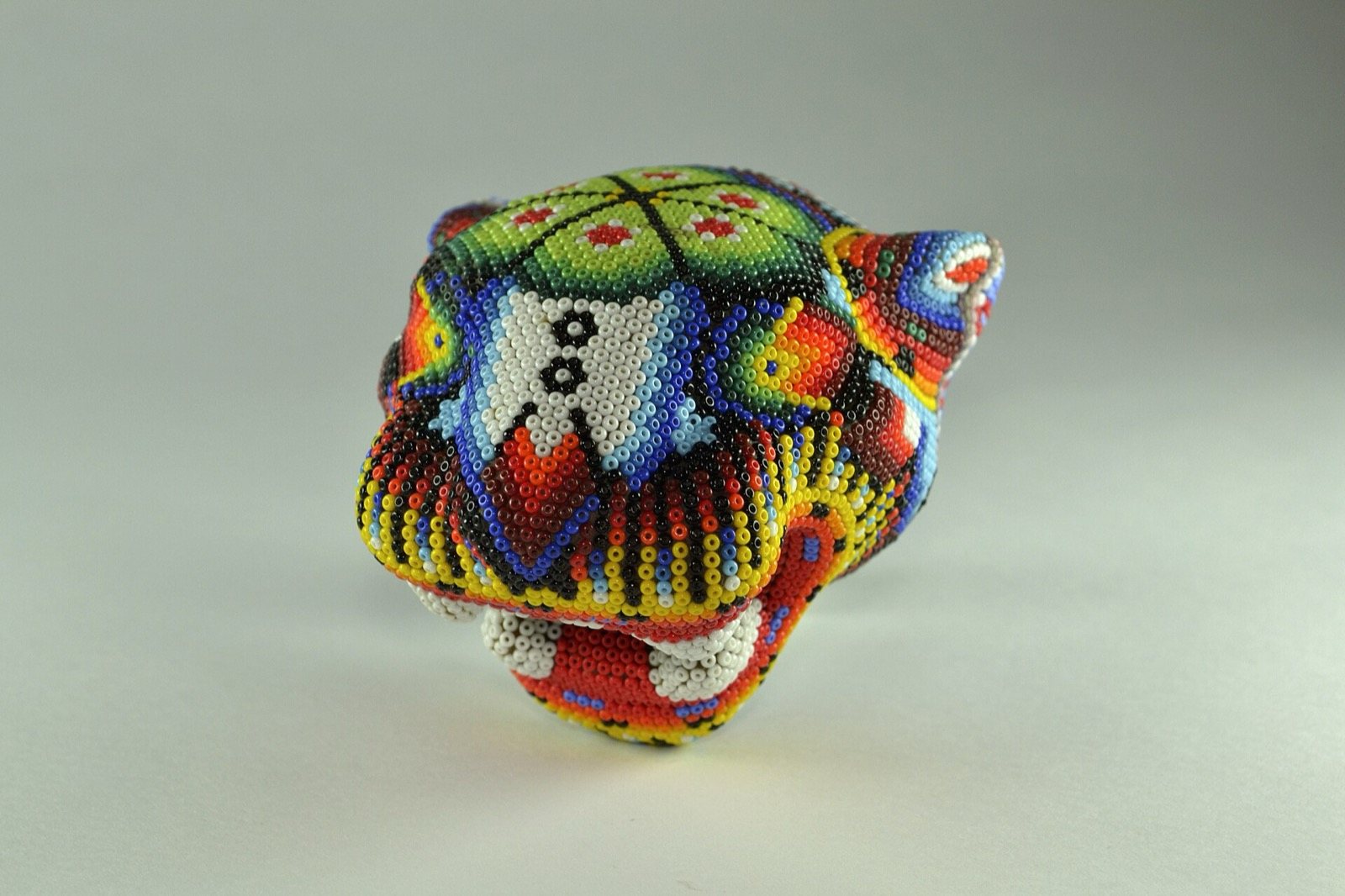 Jaguar head completely covered in colorful glass beads on a light gray background