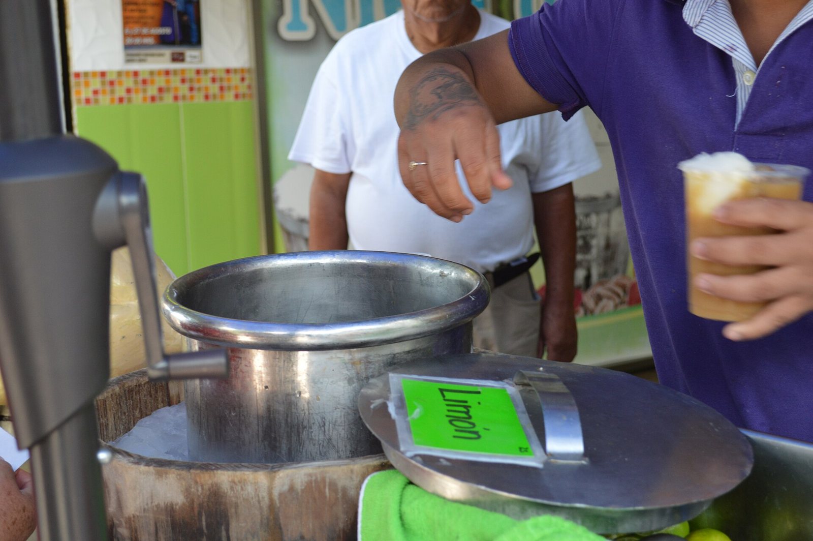 Street vendor holding a cup of tejuino topped with lime sorbet next to the sorbet churn