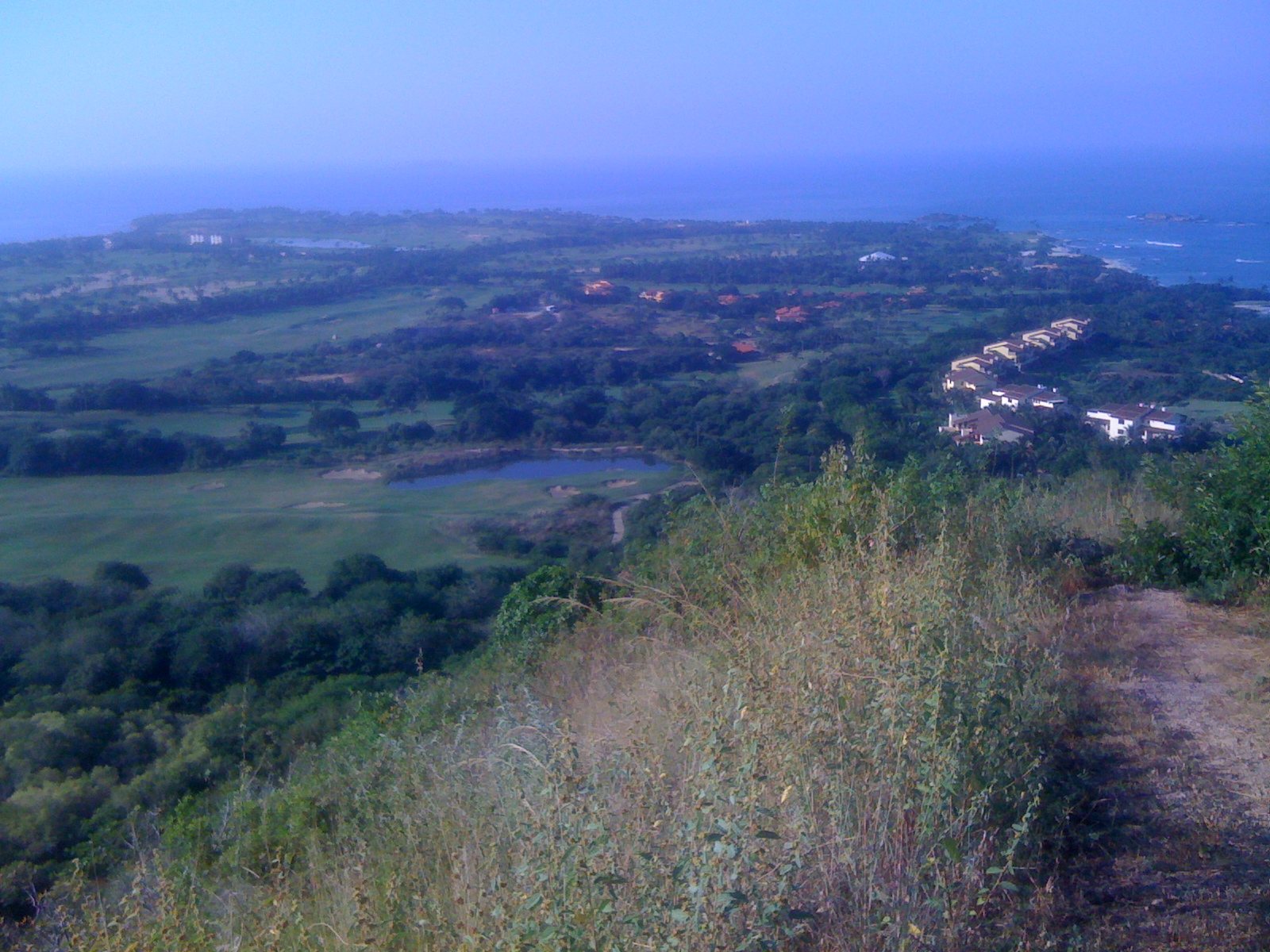 Hilltop view of the Punta Mita golf courses with a lake, villas among the trees and the ocean beyond