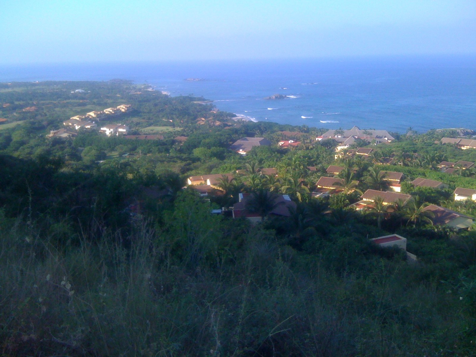 Tile-roofed villas among palm trees on the Punta Mita peninsula, with blue ocean and small islets in the distance