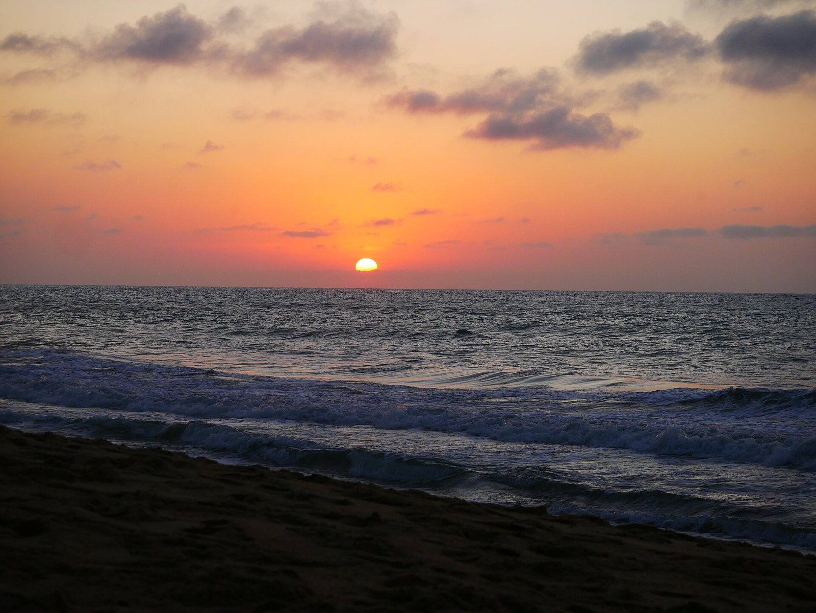 The sun setting on the Pacific horizon under an orange sky, with waves breaking on the sand at San Pancho