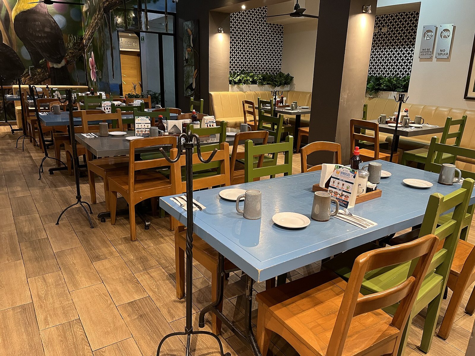Dining room at Fredy's Tucan with blue tables, green and orange wooden chairs, coffee mugs and a toucan mural on the wall