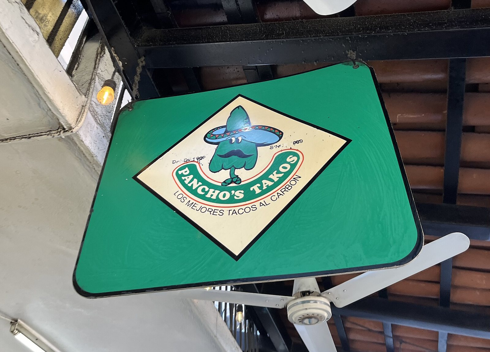 Green hanging sign for Pancho's Takos with a sombrero-wearing cartoon character and the words Los mejores tacos al carbón