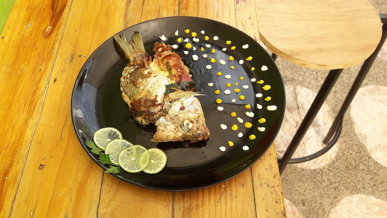 Grilled pescado zarandeado on a black plate with lime slices on a wooden table