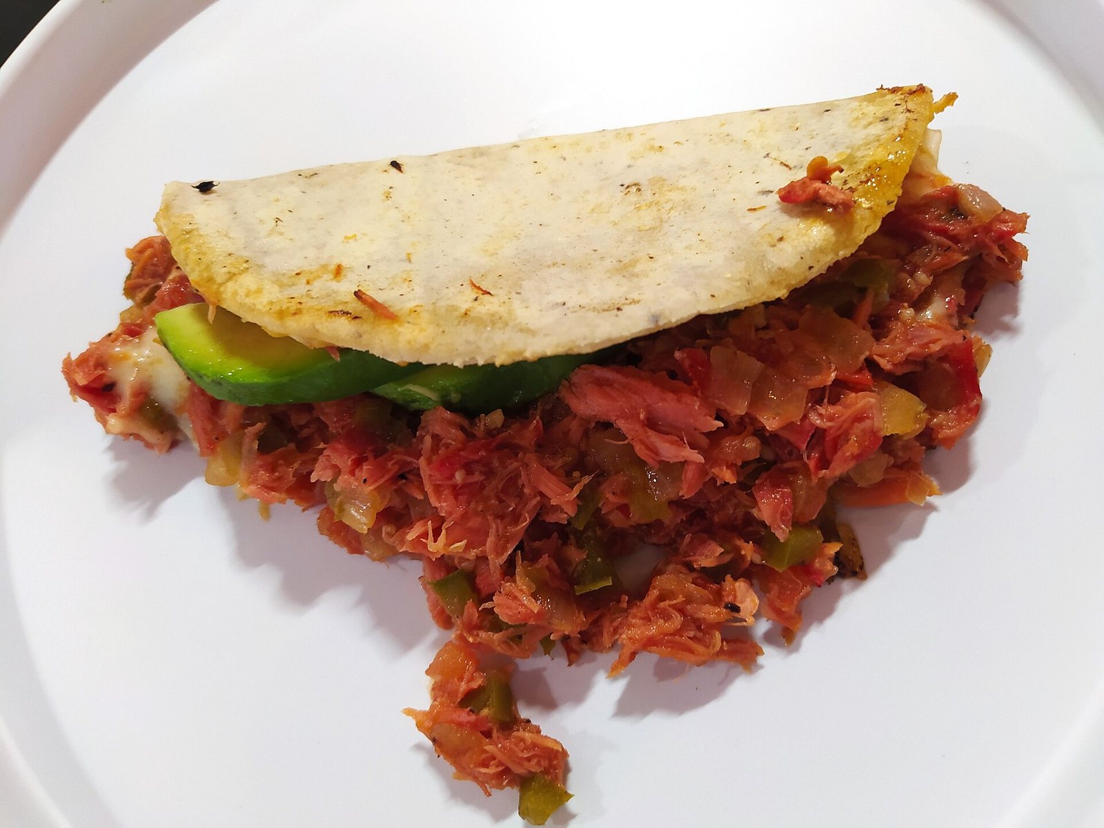 Corn tortilla quesadilla filled with marlin stewed in tomato, with a slice of avocado, on a white plate