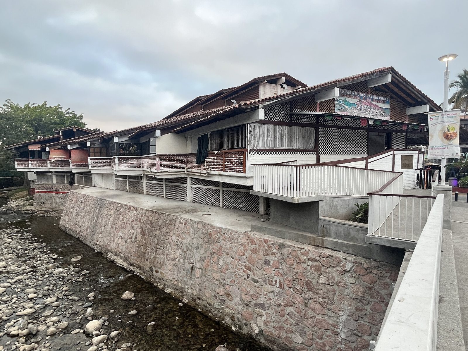 The Mercado Municipal Río Cuale building with balconies and tile roofs, set on a stone wall along the Cuale River