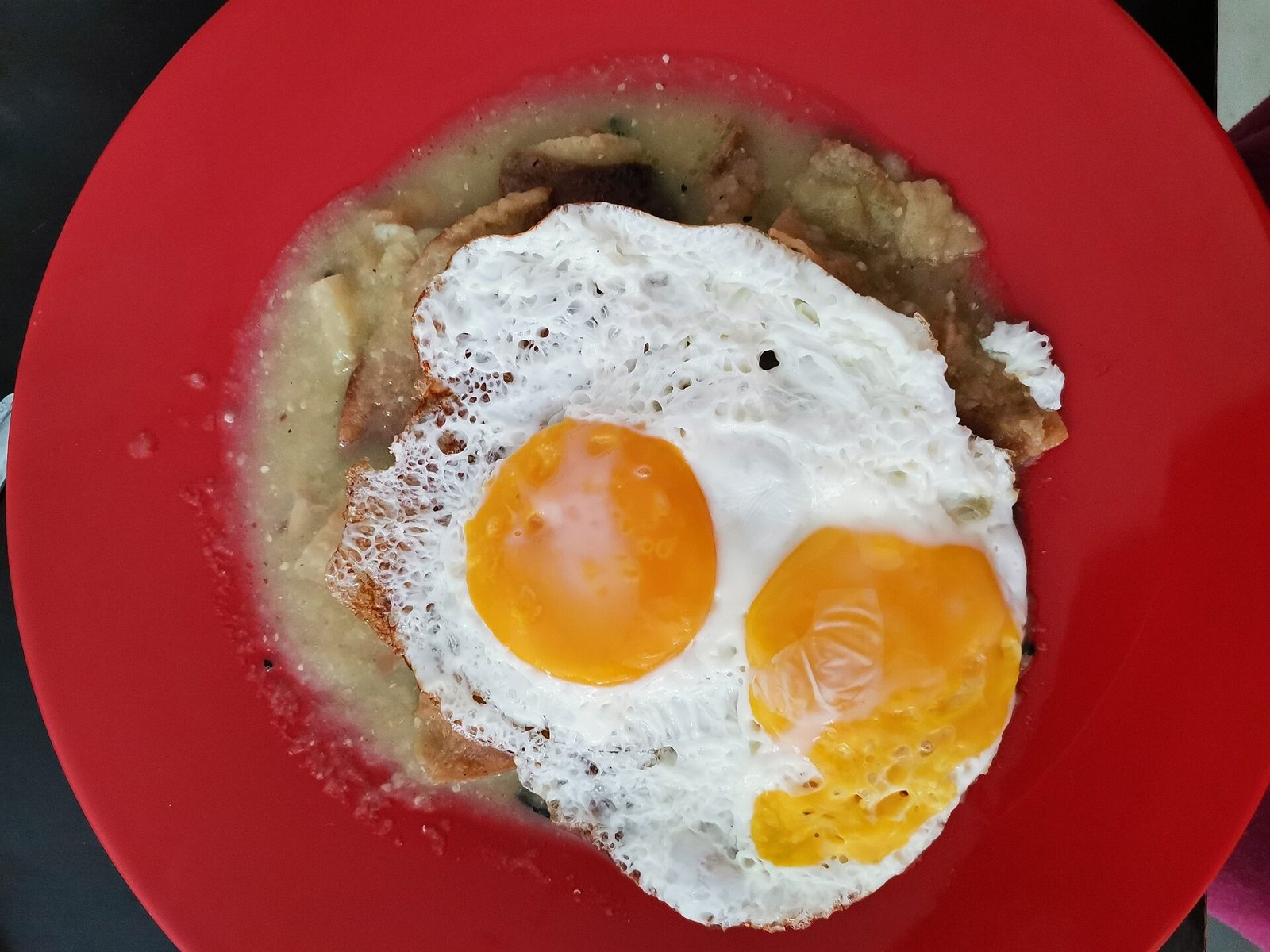 Red plate of chilaquiles in green salsa topped with two sunny-side-up eggs