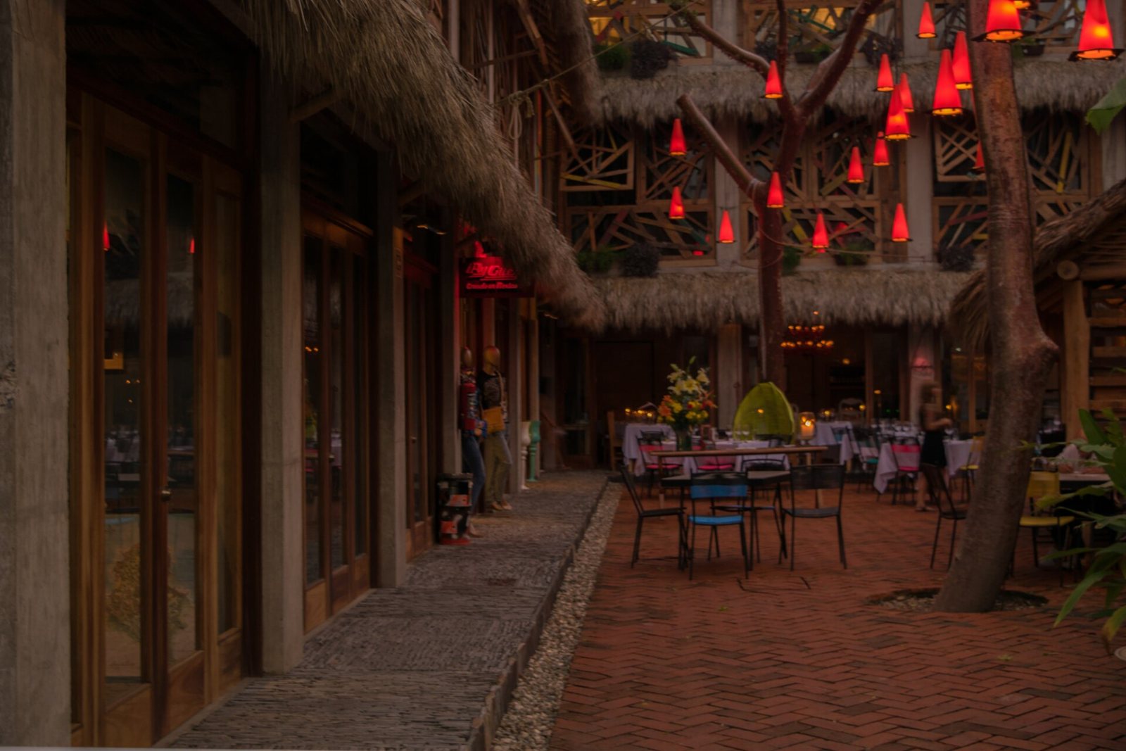 Restaurant patio in Sayulita at dusk with outdoor tables, palapa roofs, a brick floor and red lanterns hanging from a tree