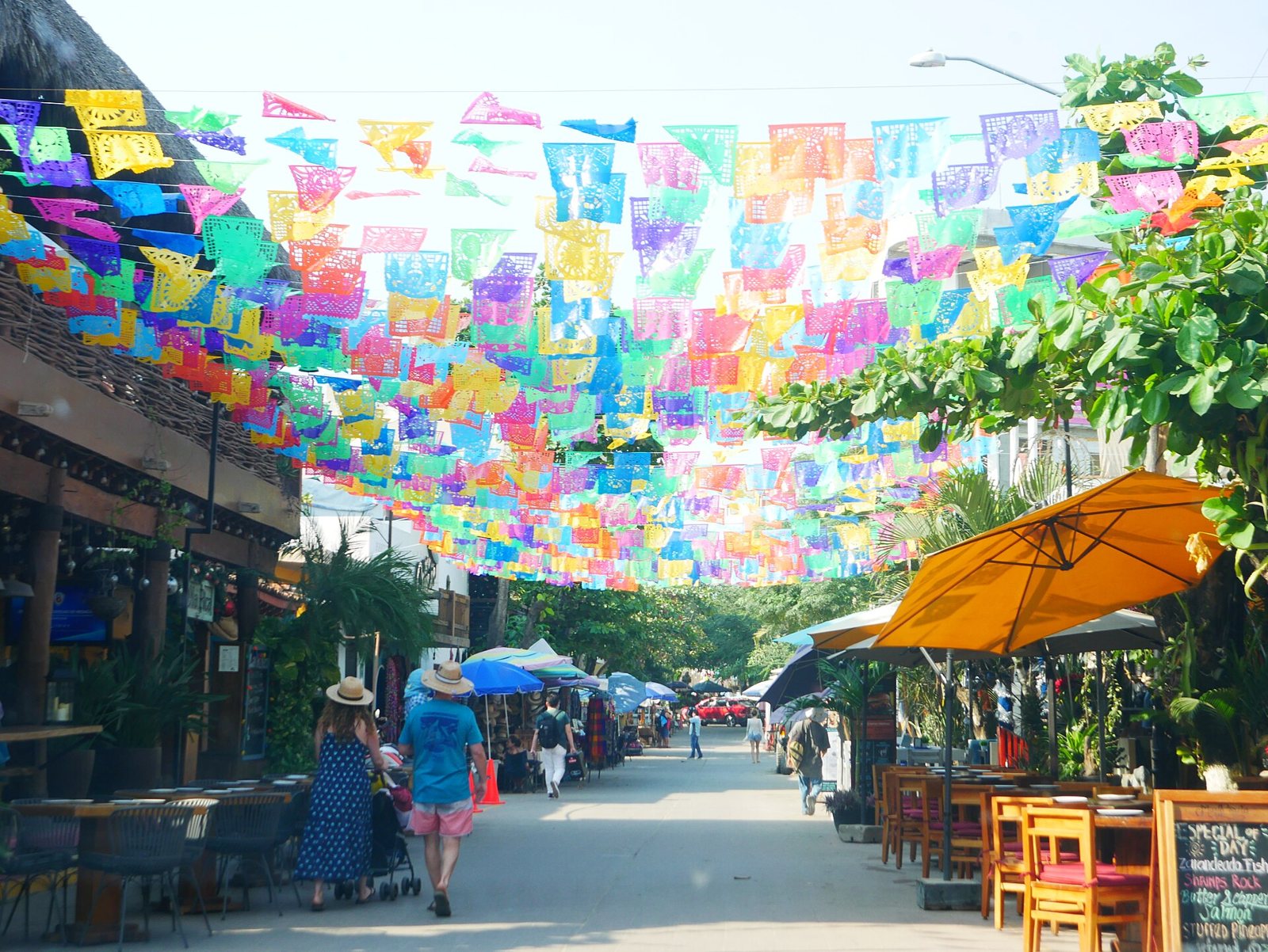 Avenida Tercer Mundo in San Pancho covered in papel picado, with restaurant tables and umbrellas along the street and people walking